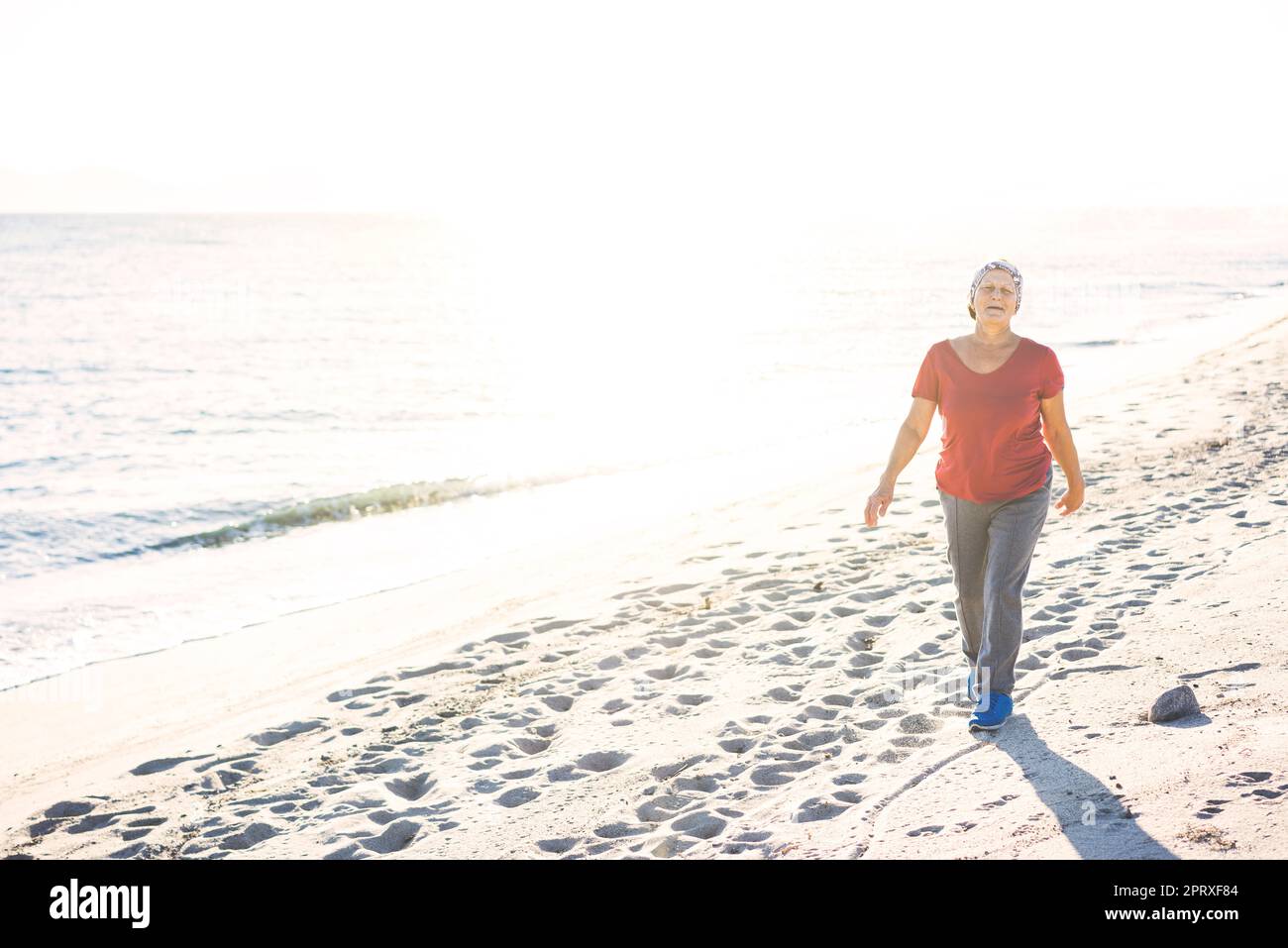 Donna anziana nel suo 70s a piedi in spiaggia, esercitandosi all'aperto Foto Stock