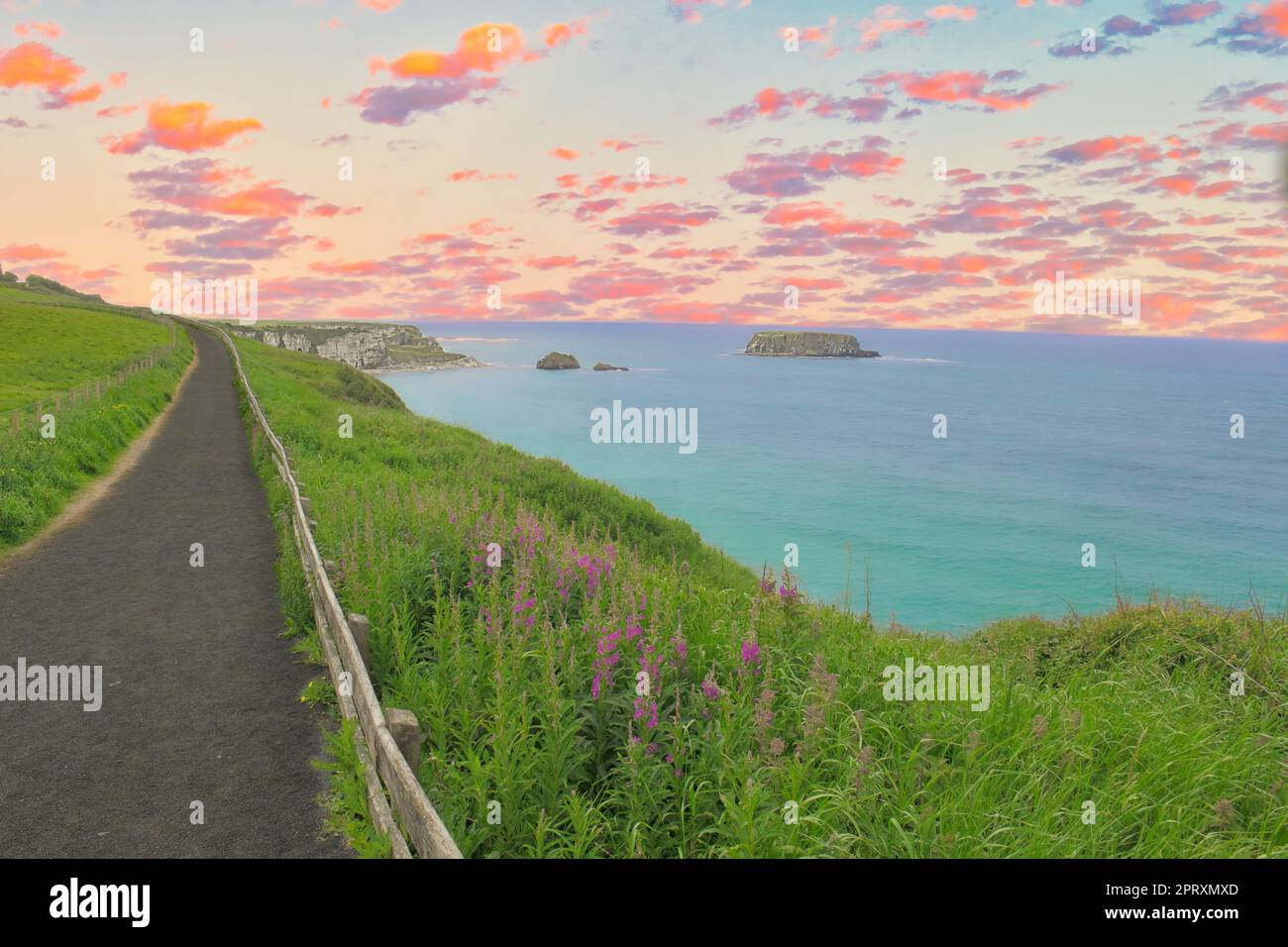 Sentieri per passeggiate ed escursioni al Carrick-a-Rede Rope Bridge, Irlanda, Regno Unito, nell'ora d'oro spettacolare cielo al tramonto e nuvole con vista sul prato e sull'oceano Foto Stock