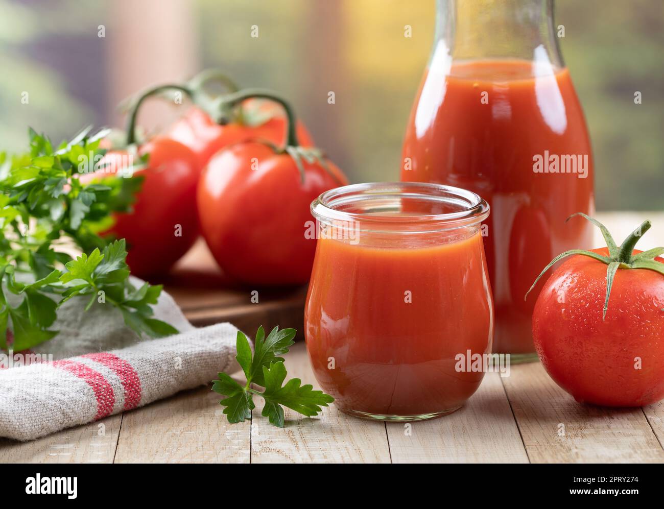 Succo di pomodoro in bicchiere e caraffa con pomodori freschi e prezzemolo su tavolo di legno Foto Stock