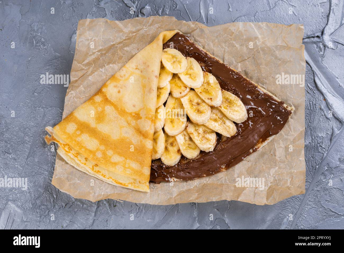 Crepes ripiene di cioccolato da spalmare e banana sulla piastra bianca. Frittelle sottili, blini. Dolce con. Foto Stock