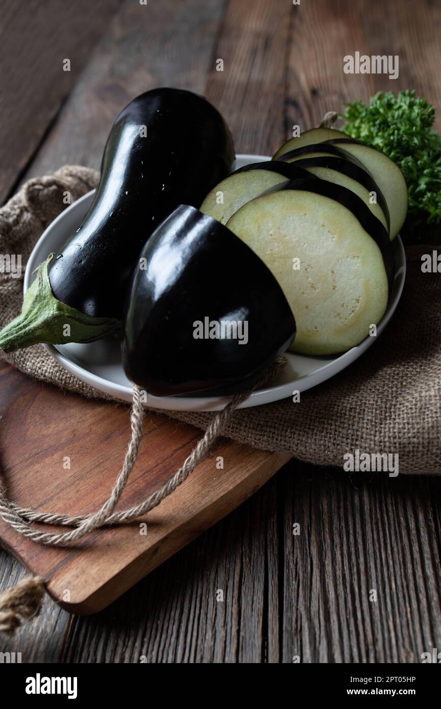 Melanzane fresche, crude e crude, intere e tagliate a fette su fondo di tavola in legno. Primo piano con spazio di copia Foto Stock