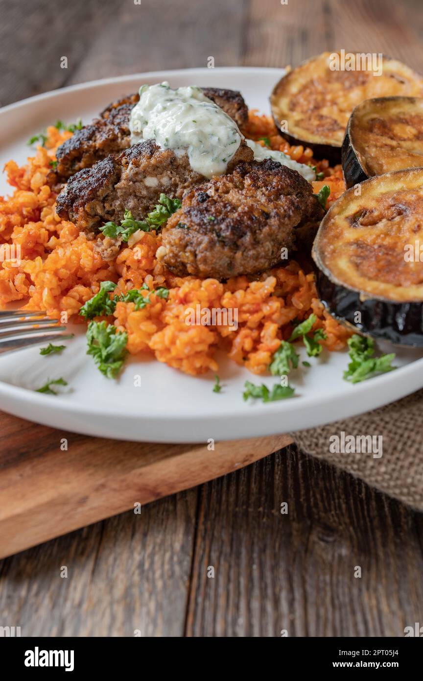 Bifteki greco, polpette di manzo o paty con riso al pomodoro e melanzane fritte e tzatziki su un piatto Foto Stock