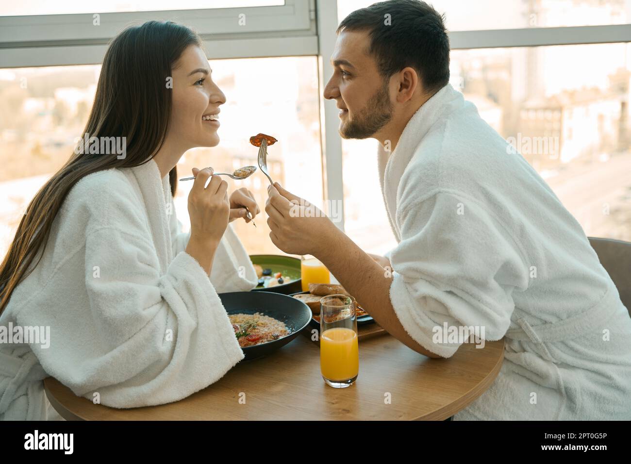 Coppia giovane e affascinante che fa una colazione romantica in un'atmosfera accogliente, ragazzi in comodi accappatoi Foto Stock