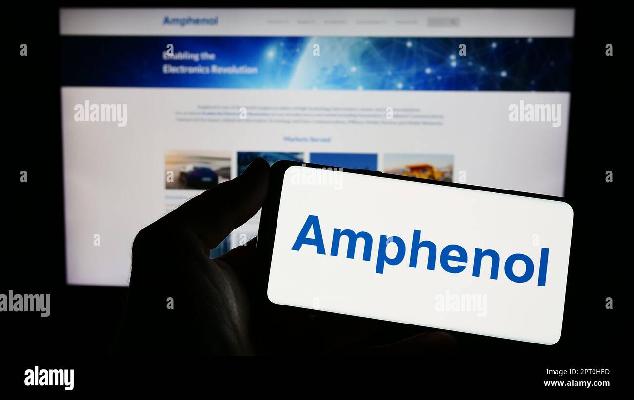 Persona che tiene lo smartphone con il logo della società di elettronica statunitense Amphenol Corporation sullo schermo di fronte al sito Web. Messa a fuoco sul display del telefono. Foto Stock