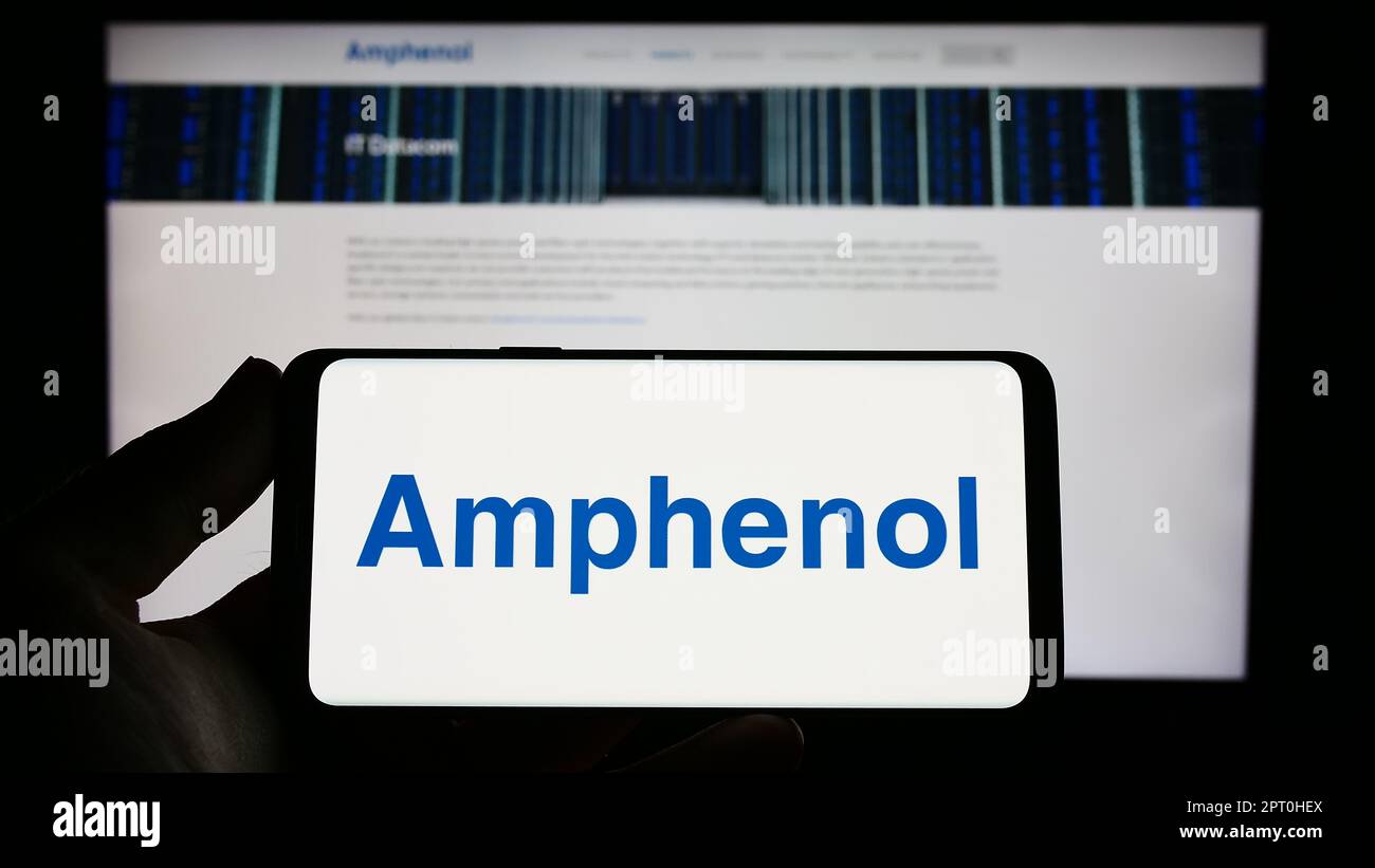 Persona che tiene il cellulare con il logo della società di elettronica americana Amphenol Corporation sullo schermo di fronte al sito web aziendale. Messa a fuoco sul display del telefono. Foto Stock