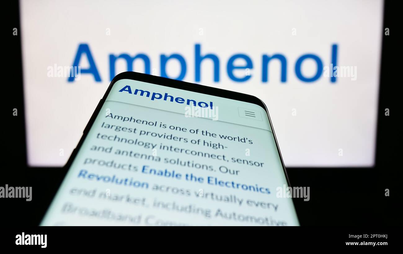 Telefono cellulare con pagina web della società di elettronica americana Amphenol Corporation sullo schermo di fronte al logo aziendale. Messa a fuoco in alto a sinistra del display del telefono. Foto Stock