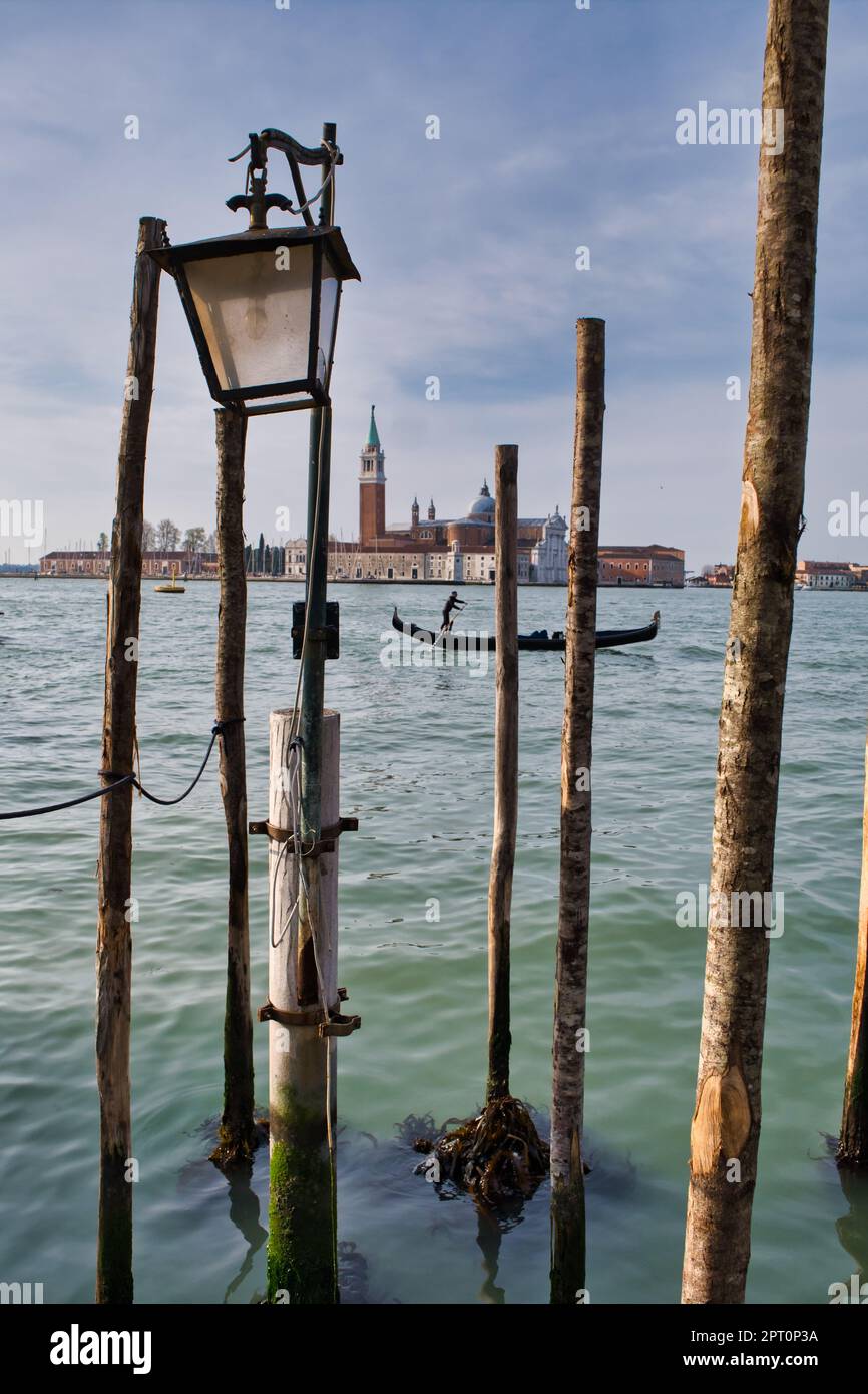 Vista di una gondola nel canale tra san Marco e san Giorgio incorniciata da pali di ormeggio a Venezia Foto Stock