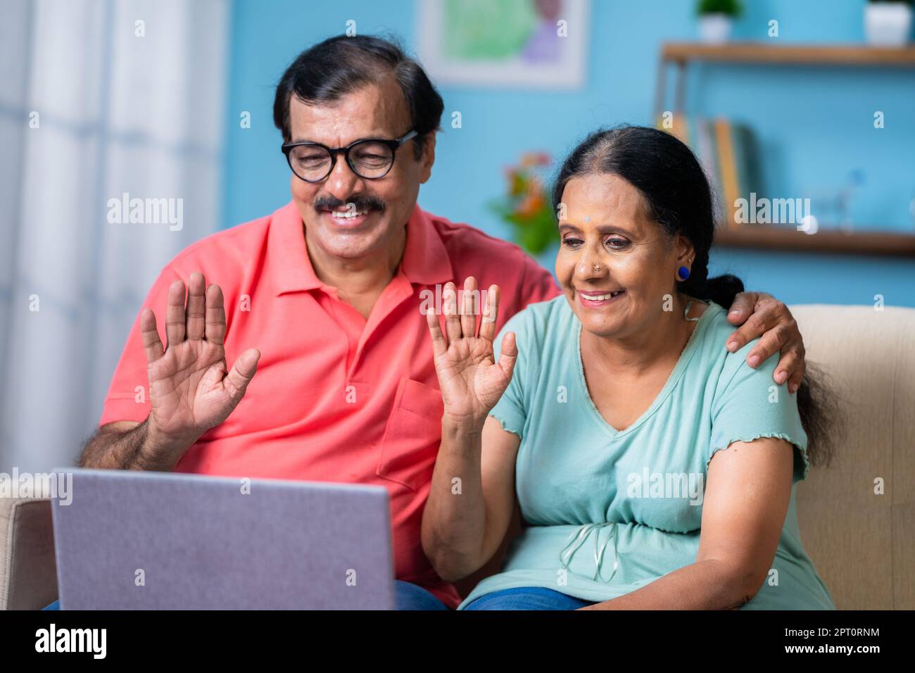 Coppia anziana indiana felice che parla di videochiamata utilizzando il computer portatile mentre si è sul divano a casa - concetto di comunicazione online, stile di vita in pensione e. Foto Stock