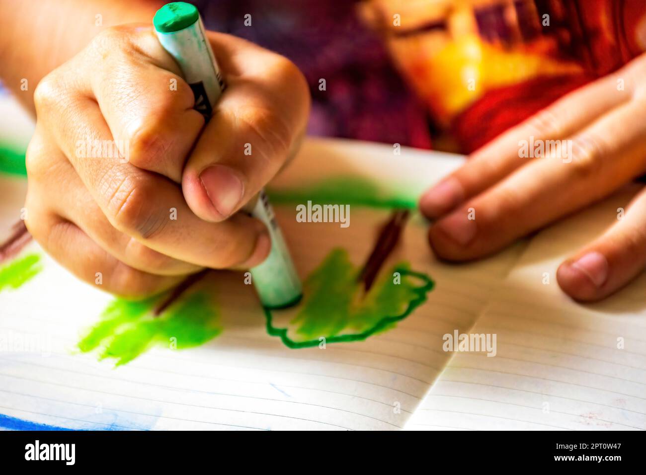 Disegno a mani di bambino con pastello su un foglio di carta illuminato dalla luce laterale dalla finestra Foto Stock