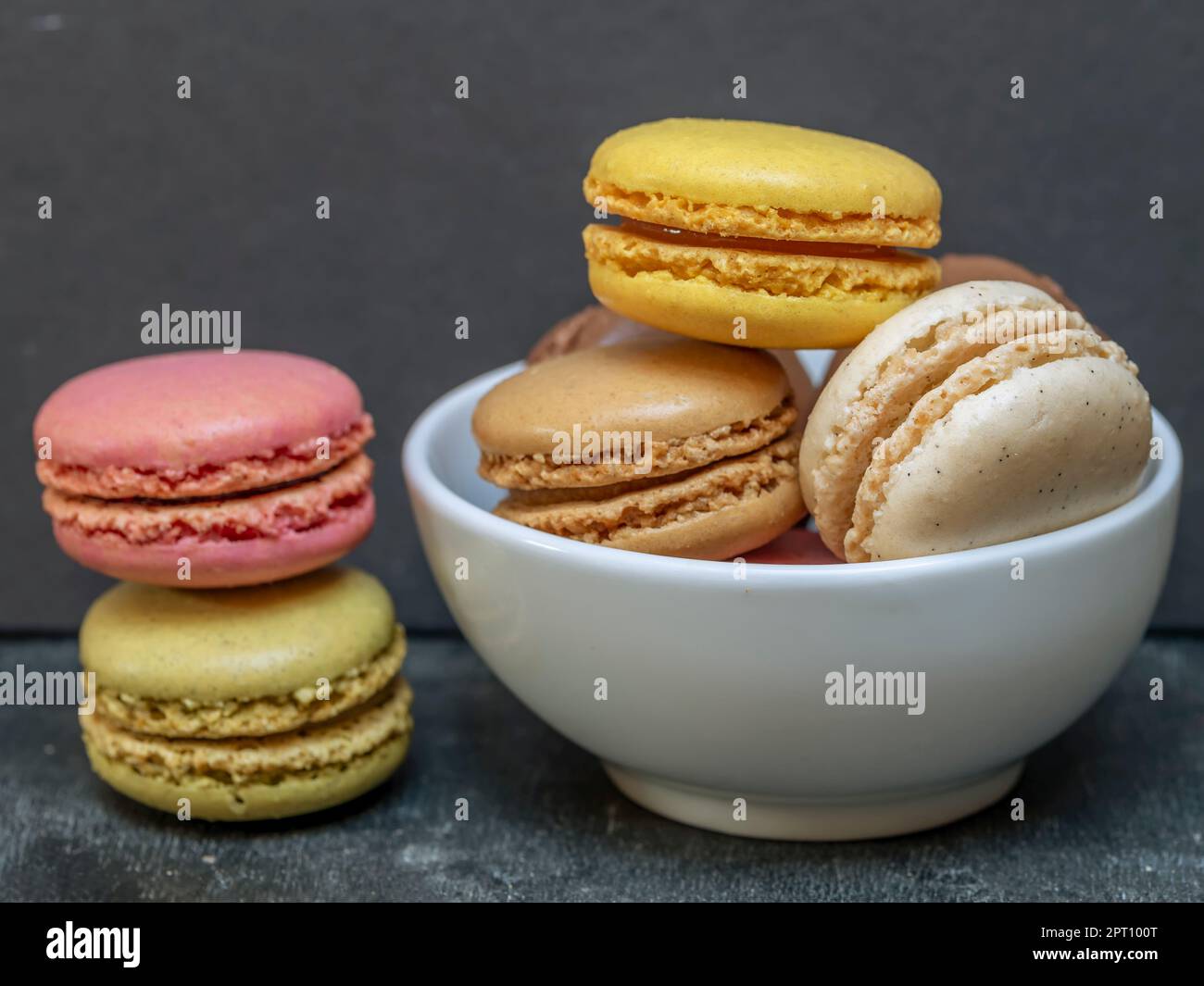 Macaron colorati in una ciotola bianca accanto a una pila di due Foto Stock