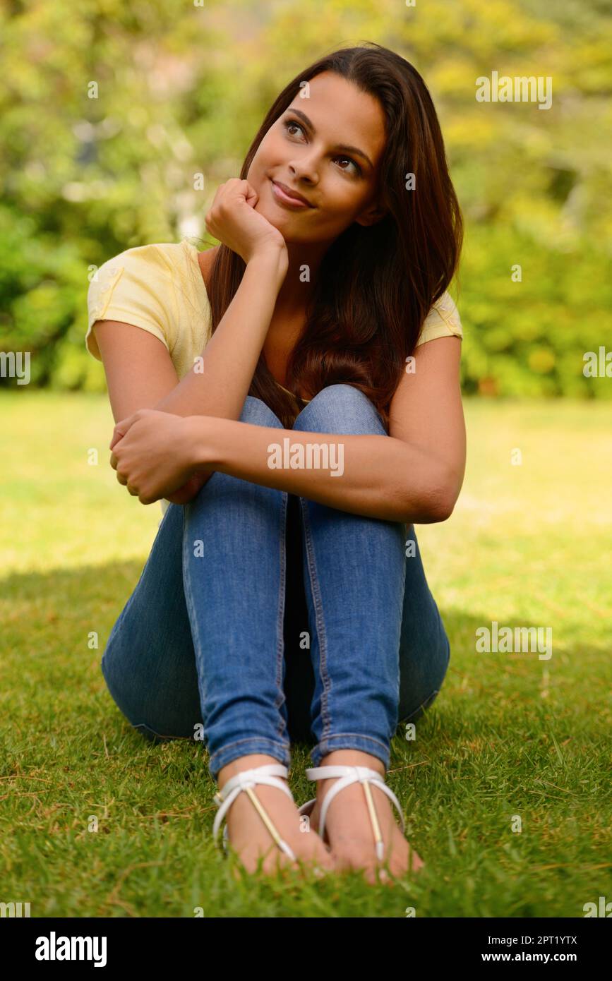 Pensare, rilassarsi e donna in un parco per la libertà, la motivazione e il sorriso sull'erba in natura. Calma, pace e ragazza con un'idea durante una vacanza o va Foto Stock