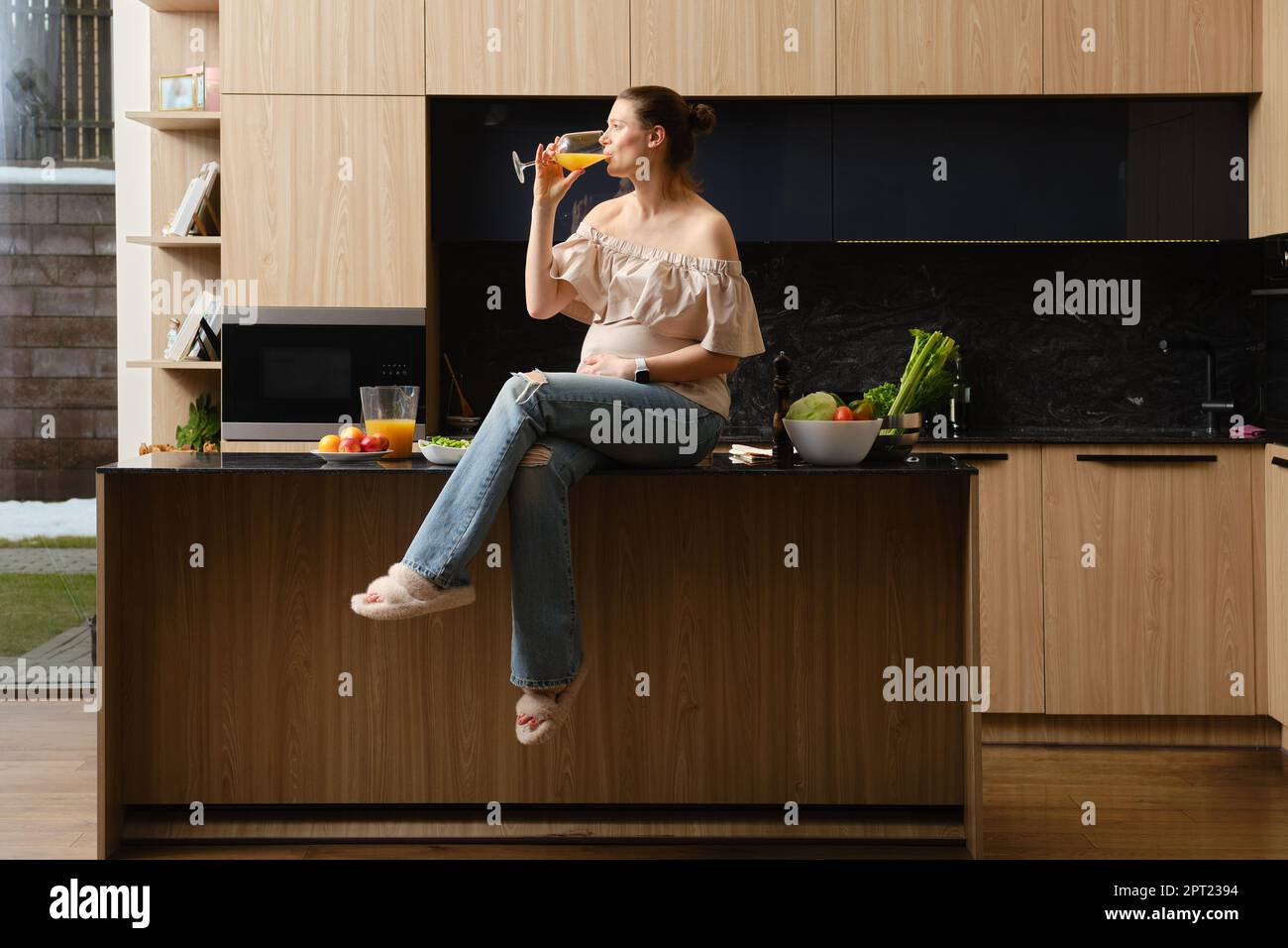 Buona guardando donna incinta beve succo seduto sul tavolo da cucina Foto Stock