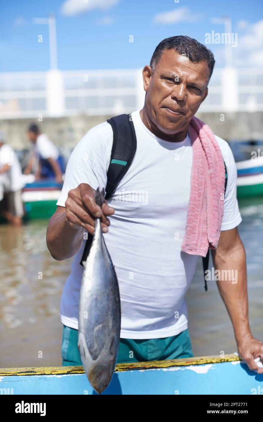 La pesca è la mia vita. Ritratto di un pescatore in piedi con un pesce accanto alla sua barca Foto Stock