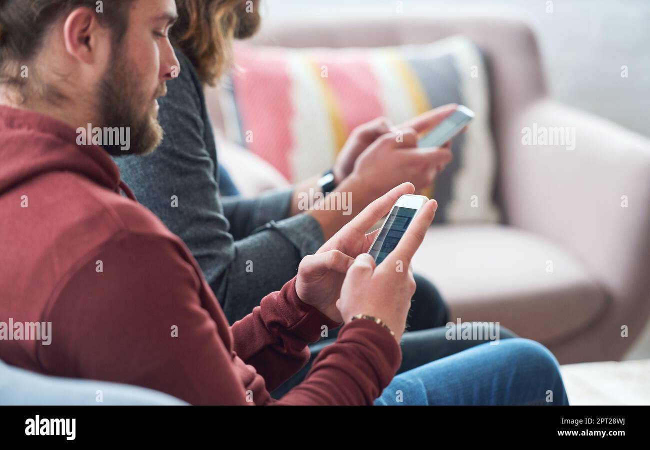 Giovane uomo che utilizza lo smartphone che naviga sui social media inviando messaggi di testo seduti sul divano con un amico. Foto Stock