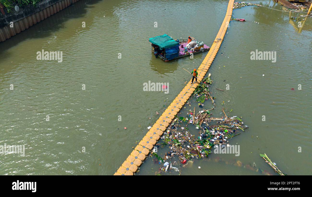 Un fiume inquinato con una trappola per la spazzatura e gli operai puliscono il fiume. Giacarta, Indonesia. Foto Stock