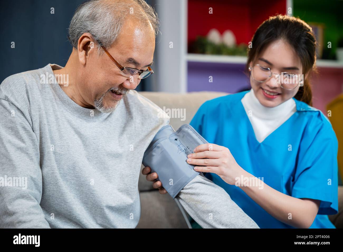 Asian nurse visit patient senior man at home she measuring arterial blood pressure on arm in living room, Doctor woman examine do checking old man cli Foto Stock
