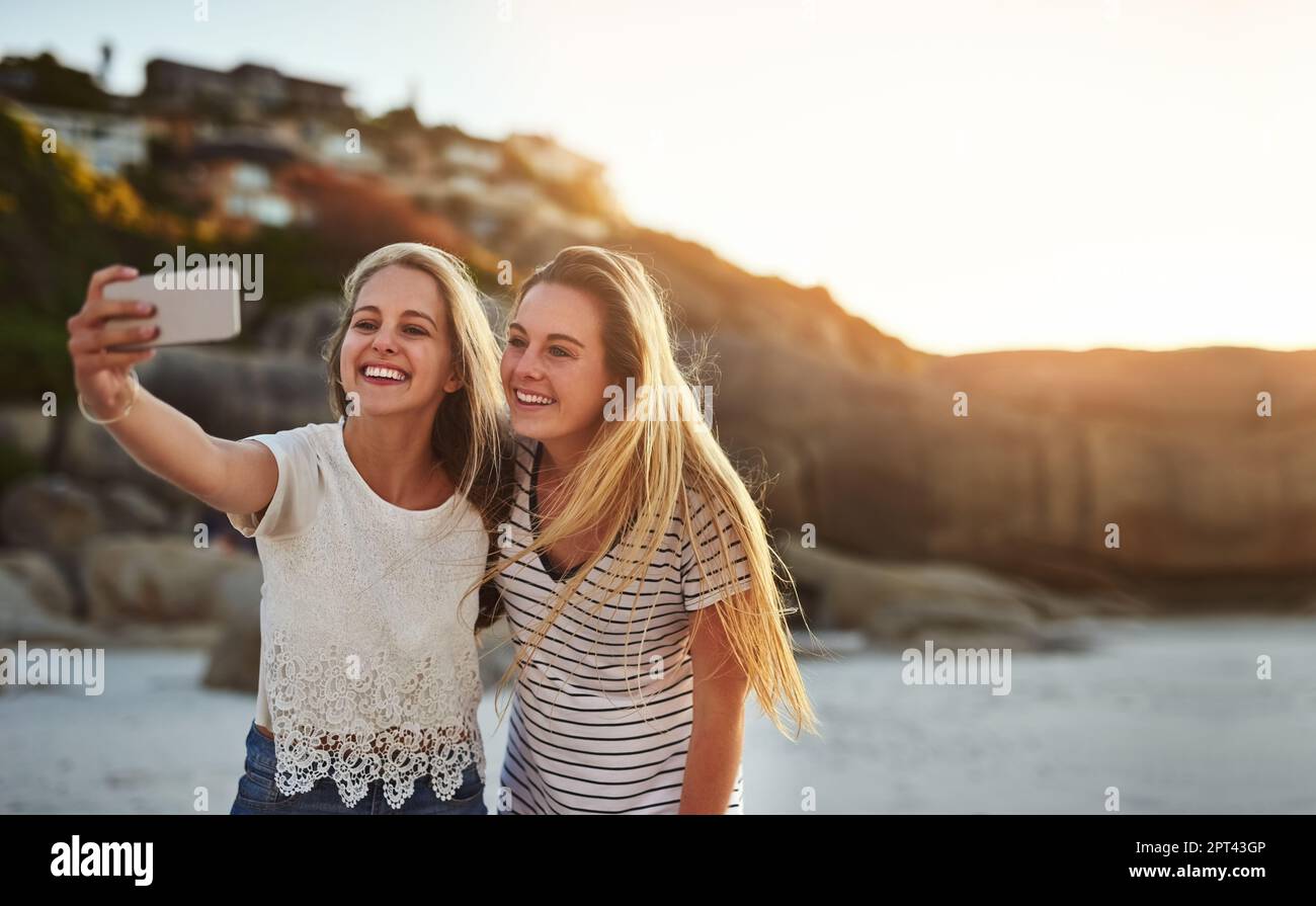 Il divertimento inizia quando la fotocamera lampeggia. due amici prendono un selfie mentre trascorrono la giornata in spiaggia Foto Stock