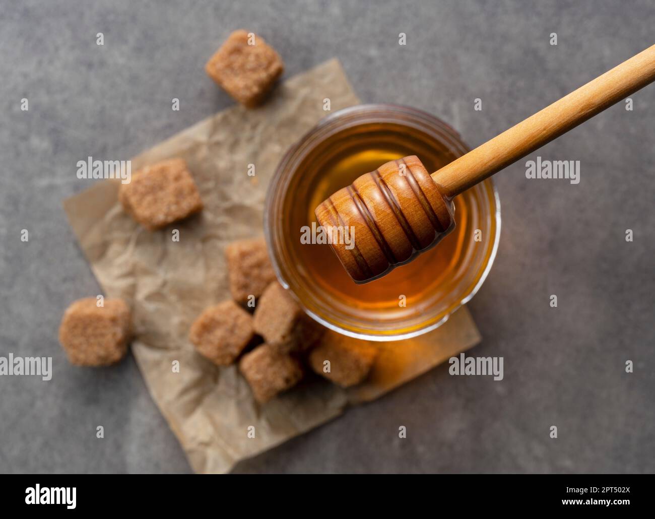 Zucchero di canna con miele e cucchiaia di miele di legno su fondo di pietra. Immagine di bellezza. Vista dall'alto. Foto Stock