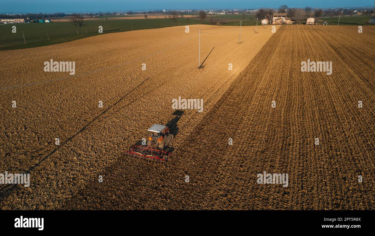 il contadino che guida un trattore cingolato trascina dietro una nuvola di polvere, arando, erpicando la rottura della crosta superficiale per facilitare la nascita e la semina di o Foto Stock