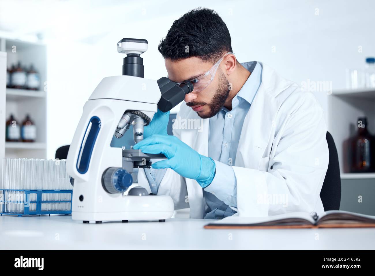 Uno scienziato medico serio seduto su una scrivania e utilizzando un microscopio per esaminare e analizzare campioni di test su vetrini. Professionista sanitario ispanico Foto Stock