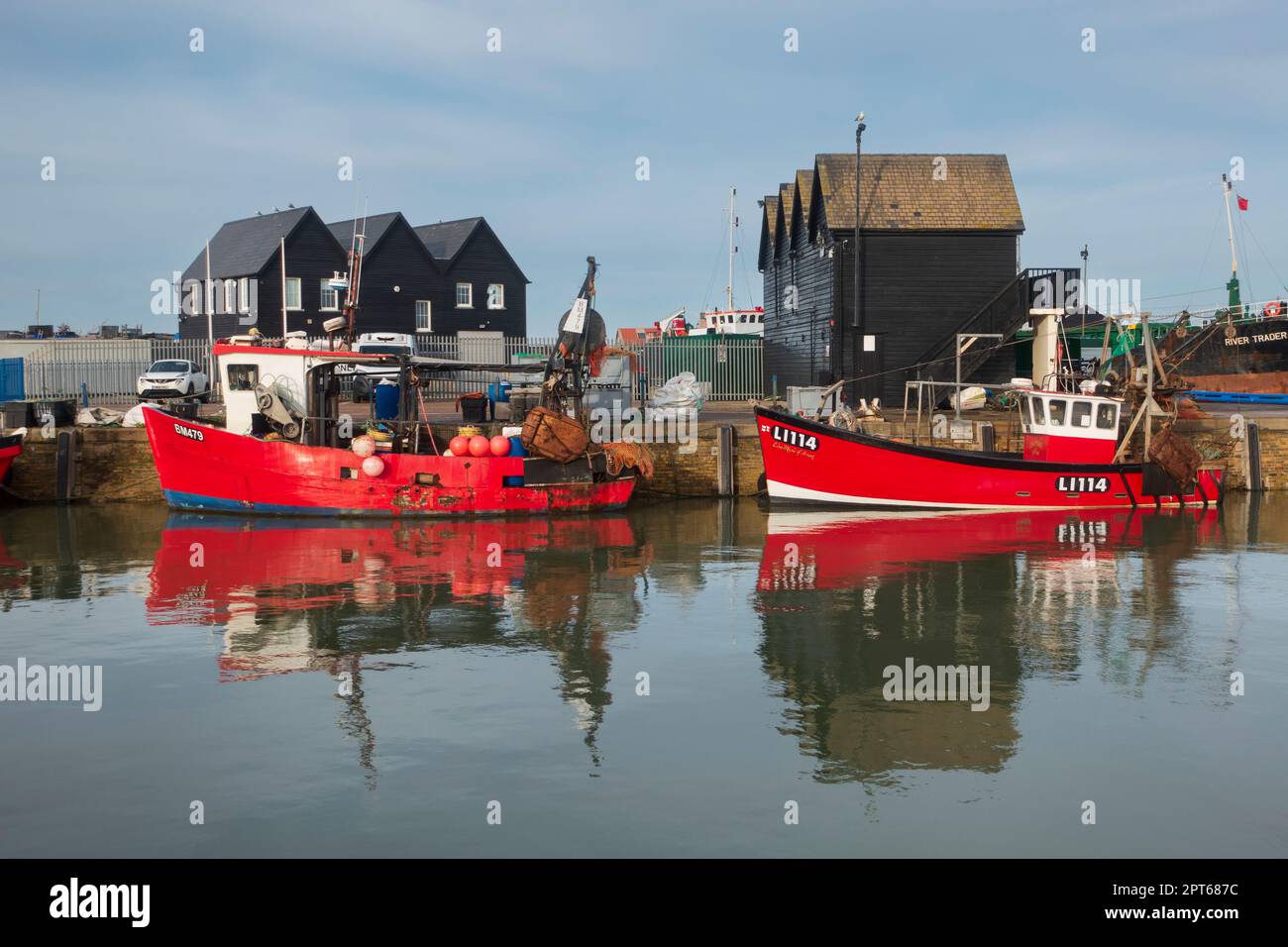 Whitstable porto, Kent. Barche da pesca legate al molo e rifugi di pescatori in background. Foto Stock