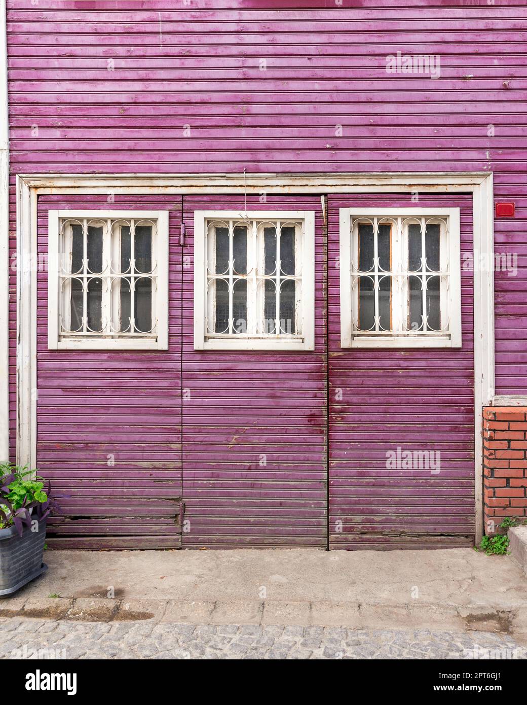 Grunge in legno intatto porte abbandonate dipinte in viola, con tre finestre in legno bianco dipinte in bianco, in un vicolo di ciottoli Foto Stock