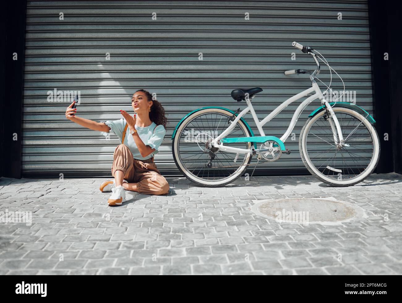 Bicicletta, strada e donna che scattano un selfie in una città che soffia un bacio in foto o foto in estate all'aperto. Libertà, moto e giovane ragazza che crea phon Foto Stock