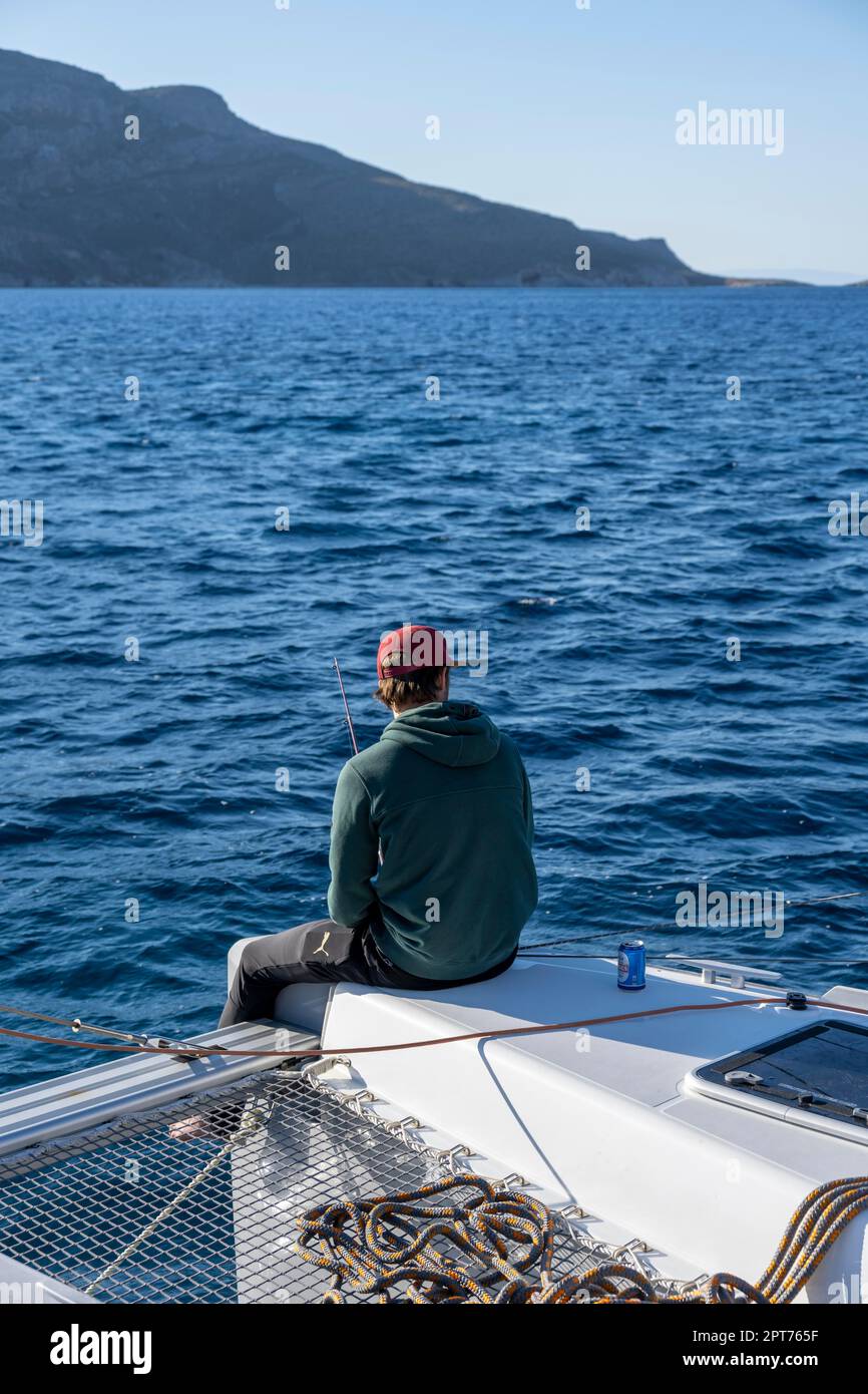 Giovane uomo che pesca su una barca a vela, vela su un catamarano a vela, Dodecaneso, Grecia Foto Stock