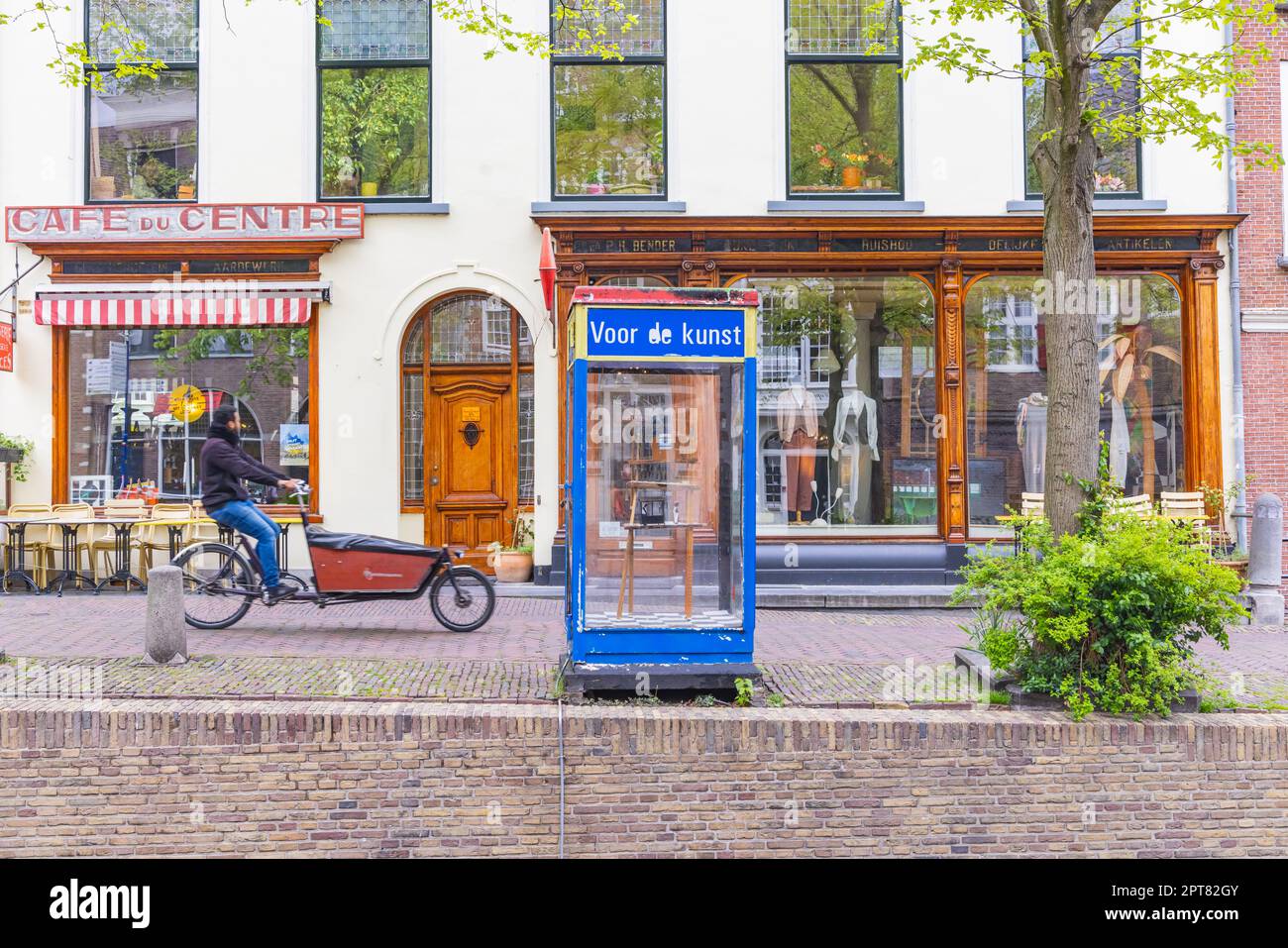 Europa, Paesi Bassi, Olanda del Sud, Delft. Aprile 25, 2022. Piccoli negozi e uomo in bicicletta da carico nella città di Delft. Foto Stock
