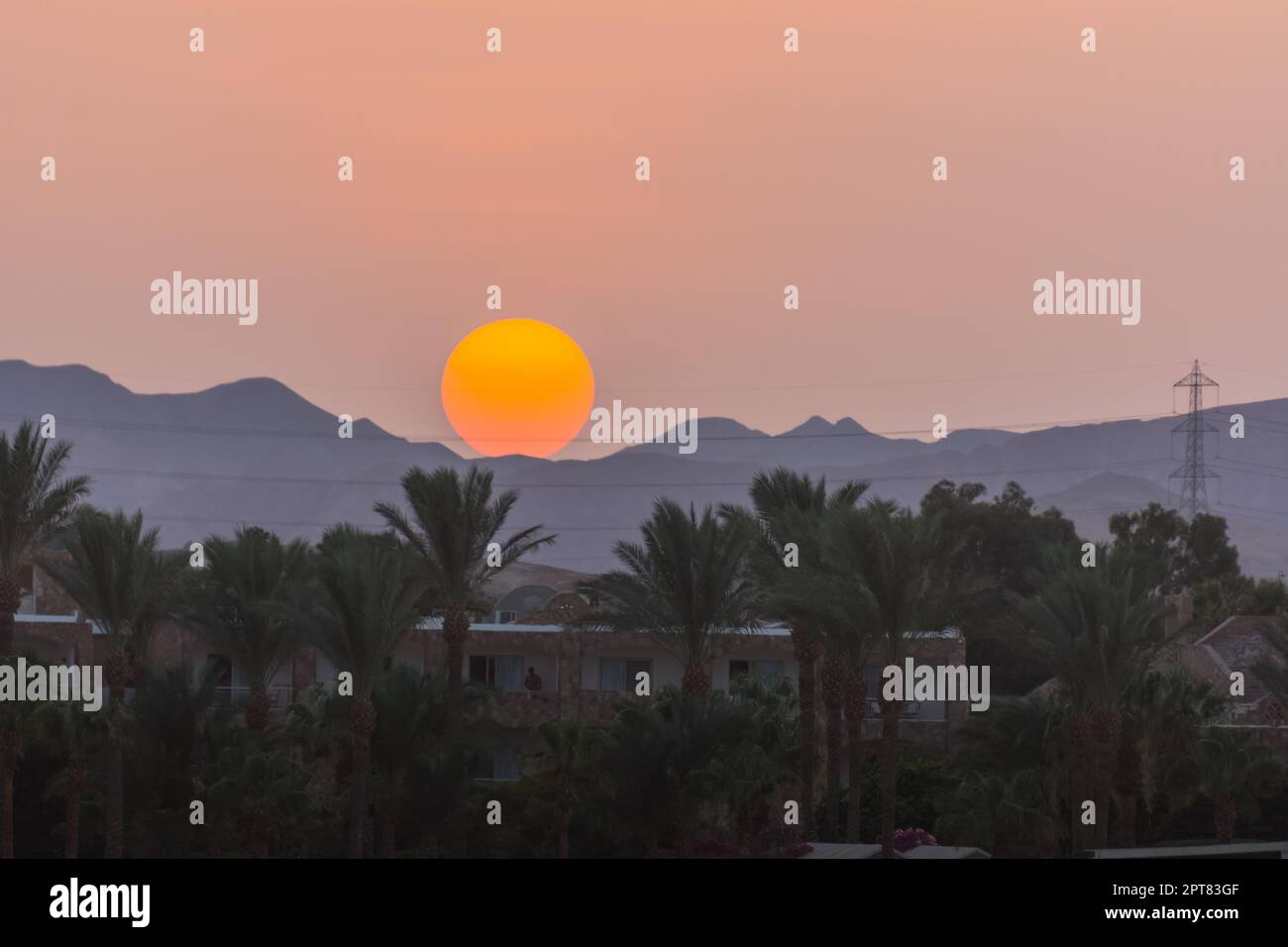 grande sole arancione sulle montagne con palme al tramonto in egitto Foto Stock