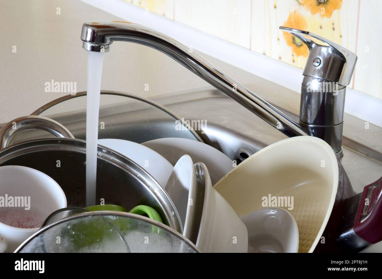 I piatti sporchi e gli elettrodomestici da cucina non lavati si trovano nell'acqua di schiuma sotto un rubinetto da un rubinetto della cucina Foto Stock