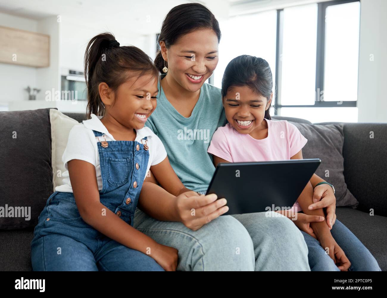 Madre e bambini felici con il tablet digitale guardare video divertenti e film. o giochi sul divano di casa. La famiglia si diverti a guardare i fumetti con la tecnologia wi Foto Stock