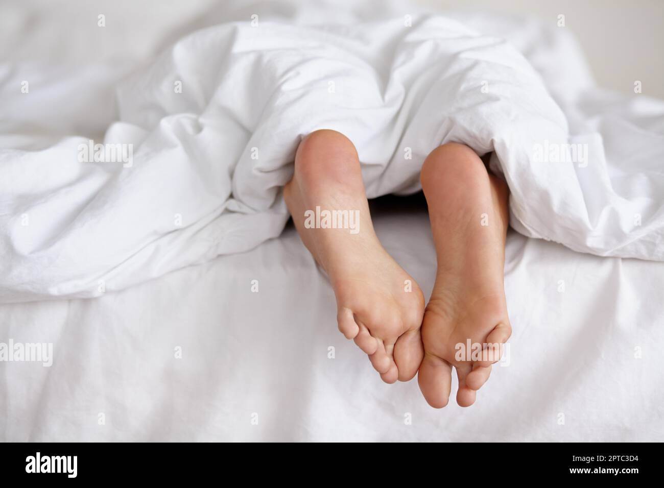 Sguazzanti tette di veglia. un paio di piedi di donna che scopano da sotto le lenzuola di un letto Foto Stock