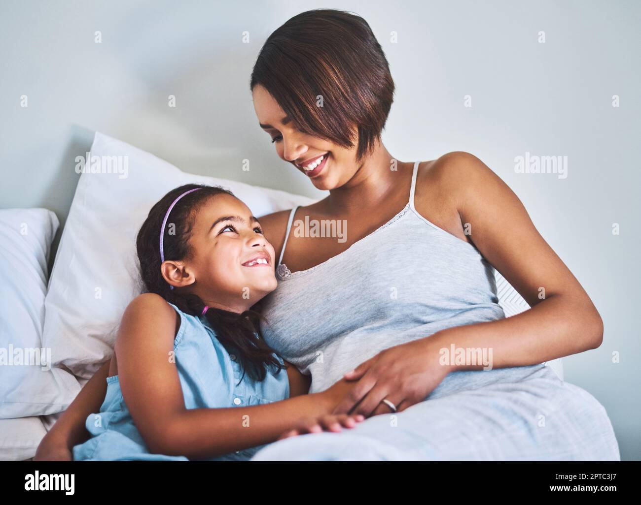 Tanto amore per i miei figli. una ragazza allegra che si rilassa sul letto con la madre incinta a casa durante il giorno Foto Stock