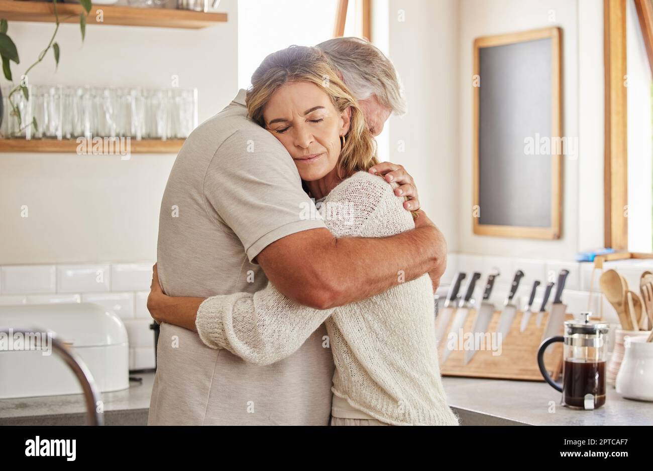 Coppia, anziani e abbraccio in cucina in casa insieme, romanticismo e amore. Cura, uomo e donna in pensione amore, matrimonio e abbraccio in triste momento per Foto Stock