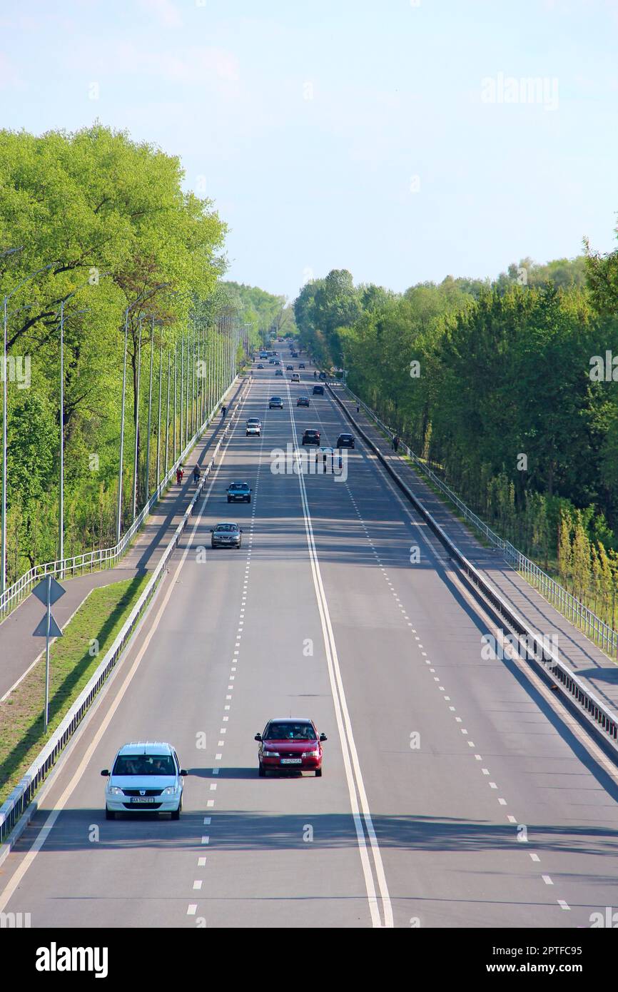 Panorama dell'autostrada con auto e alberi verdi sui lati della strada. Strada ad alta velocità. Auto in autostrada. Strada asfaltata con striscia divisoria e sottogro Foto Stock