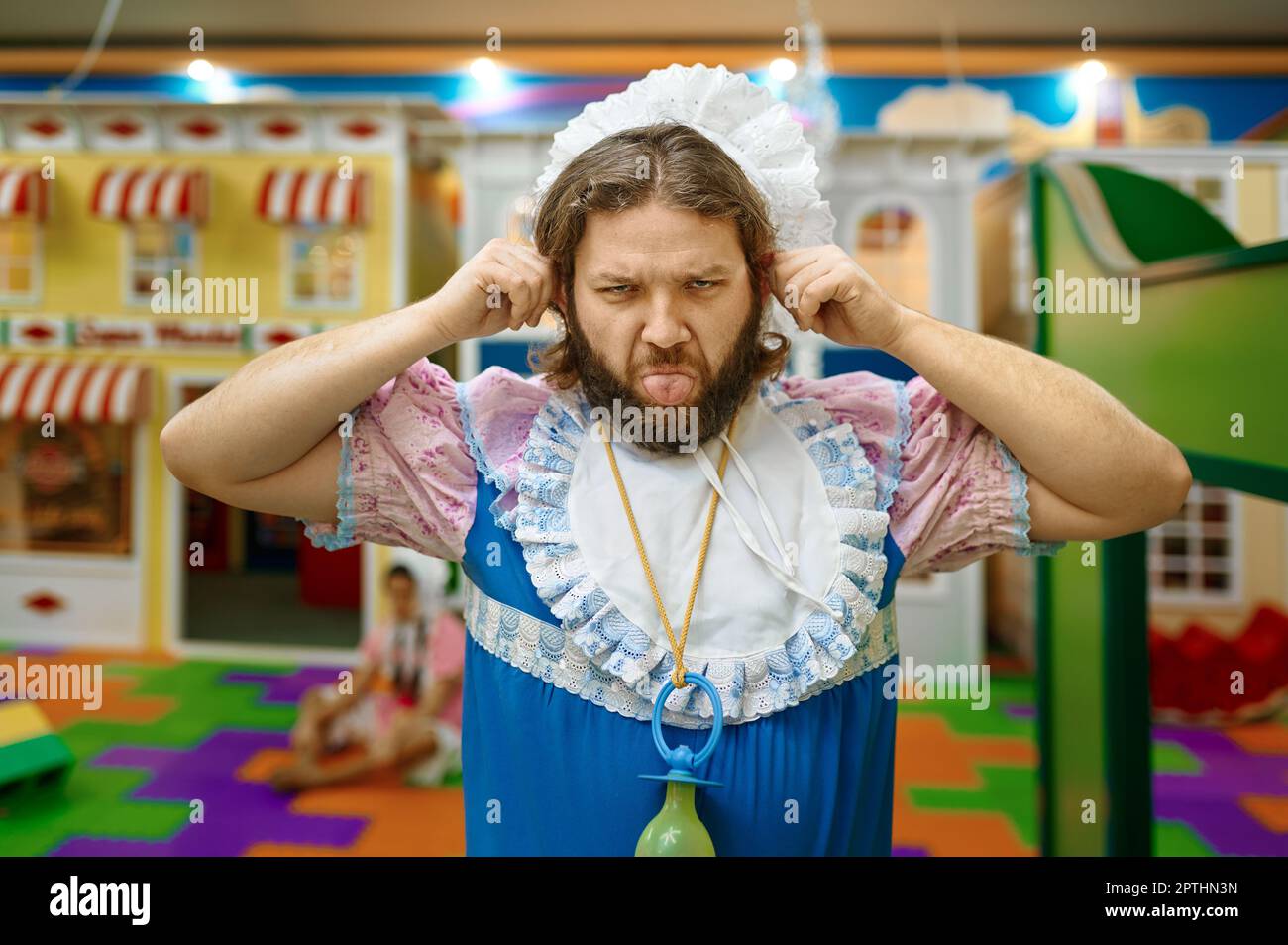 Uomo divertente come il bambino piccolo che brulda con le mani e la lingua sopra il parco giochi di divertimento dei bambini Foto Stock