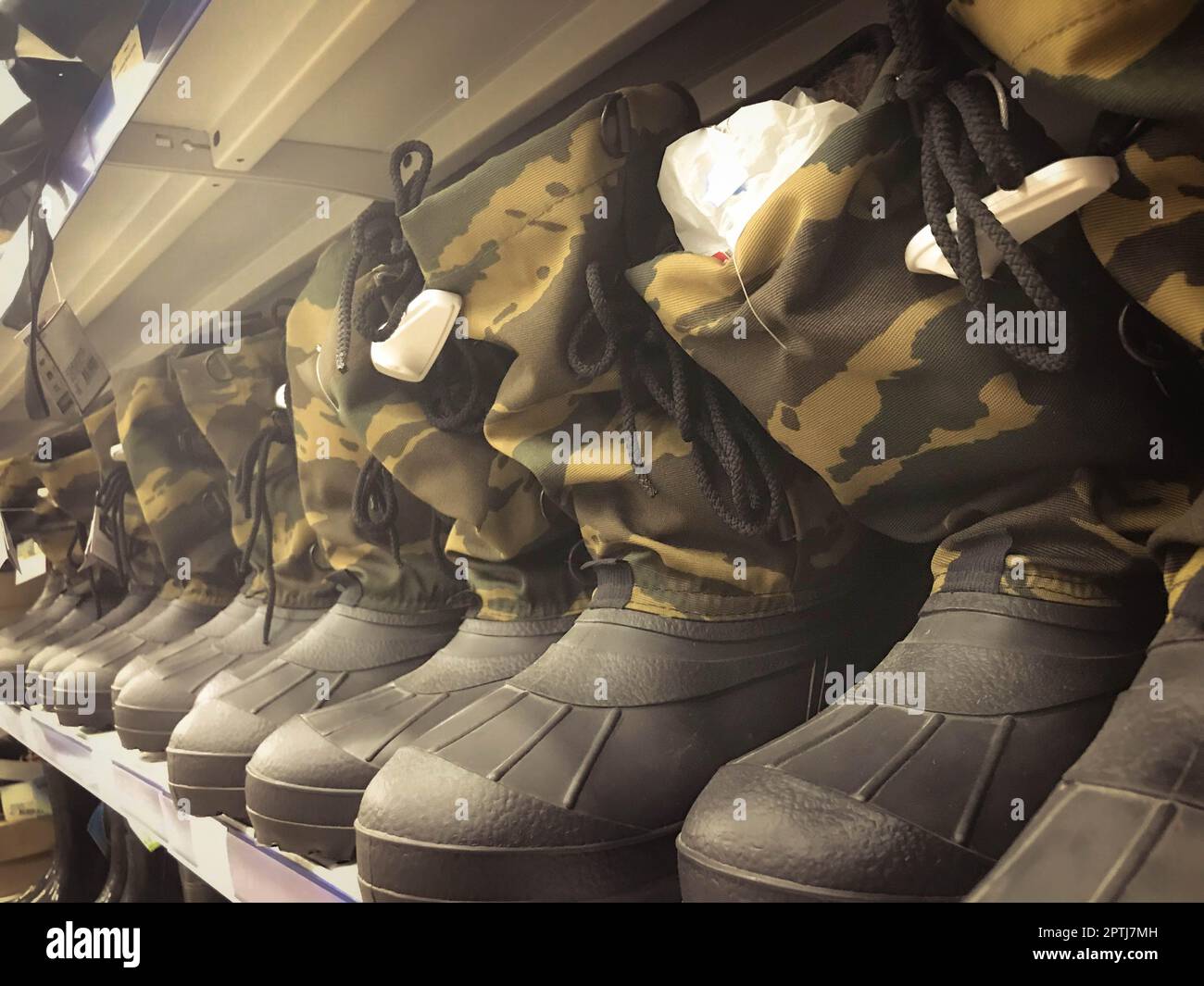 Stivali militari in gomma da uomo, scarpe in colori protettivi cachi in fila sullo scaffale del magazzino, negozio. Foto Stock