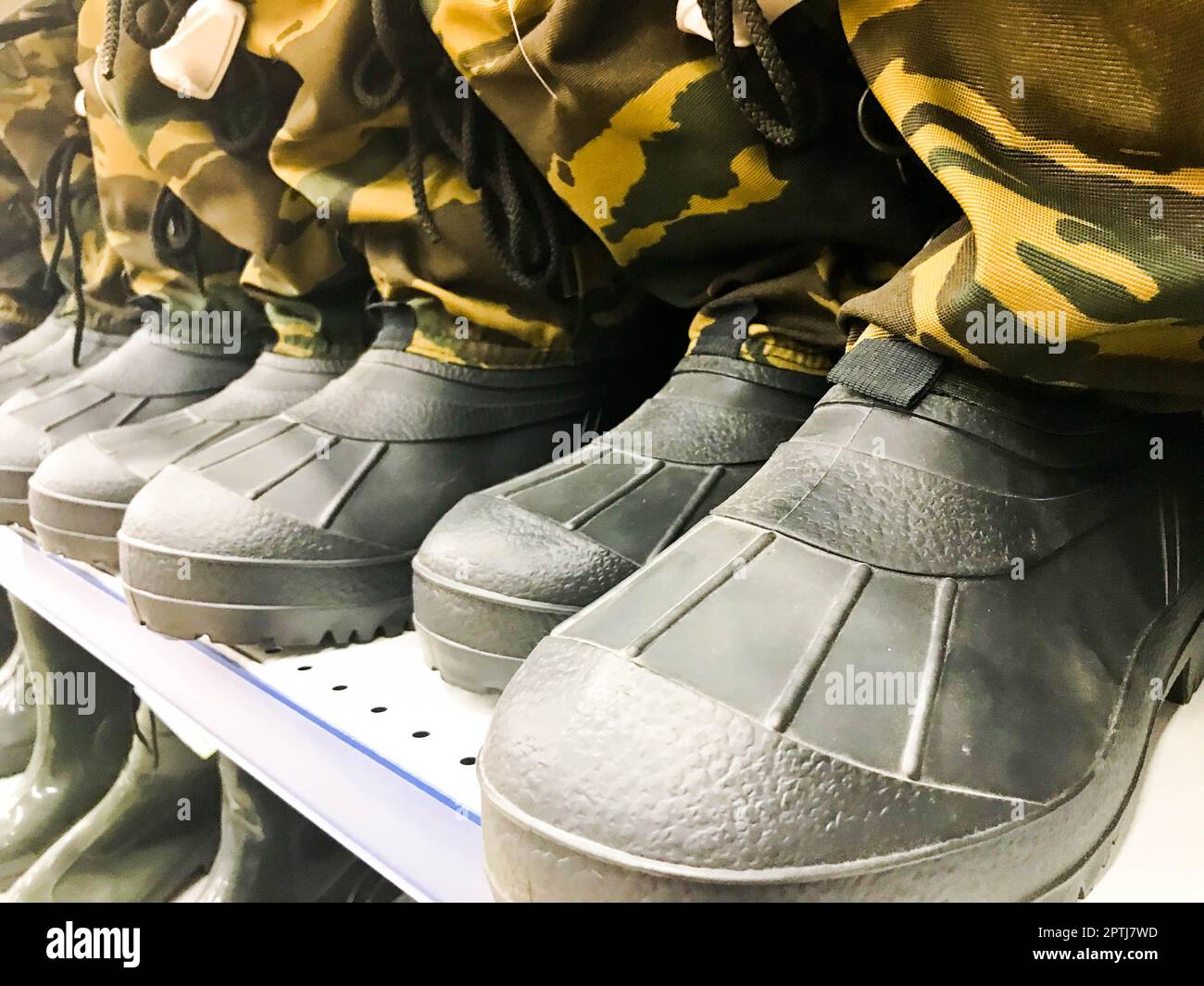 Stivali militari in gomma da uomo, scarpe in colori protettivi cachi in fila sullo scaffale del magazzino, negozio. Foto Stock