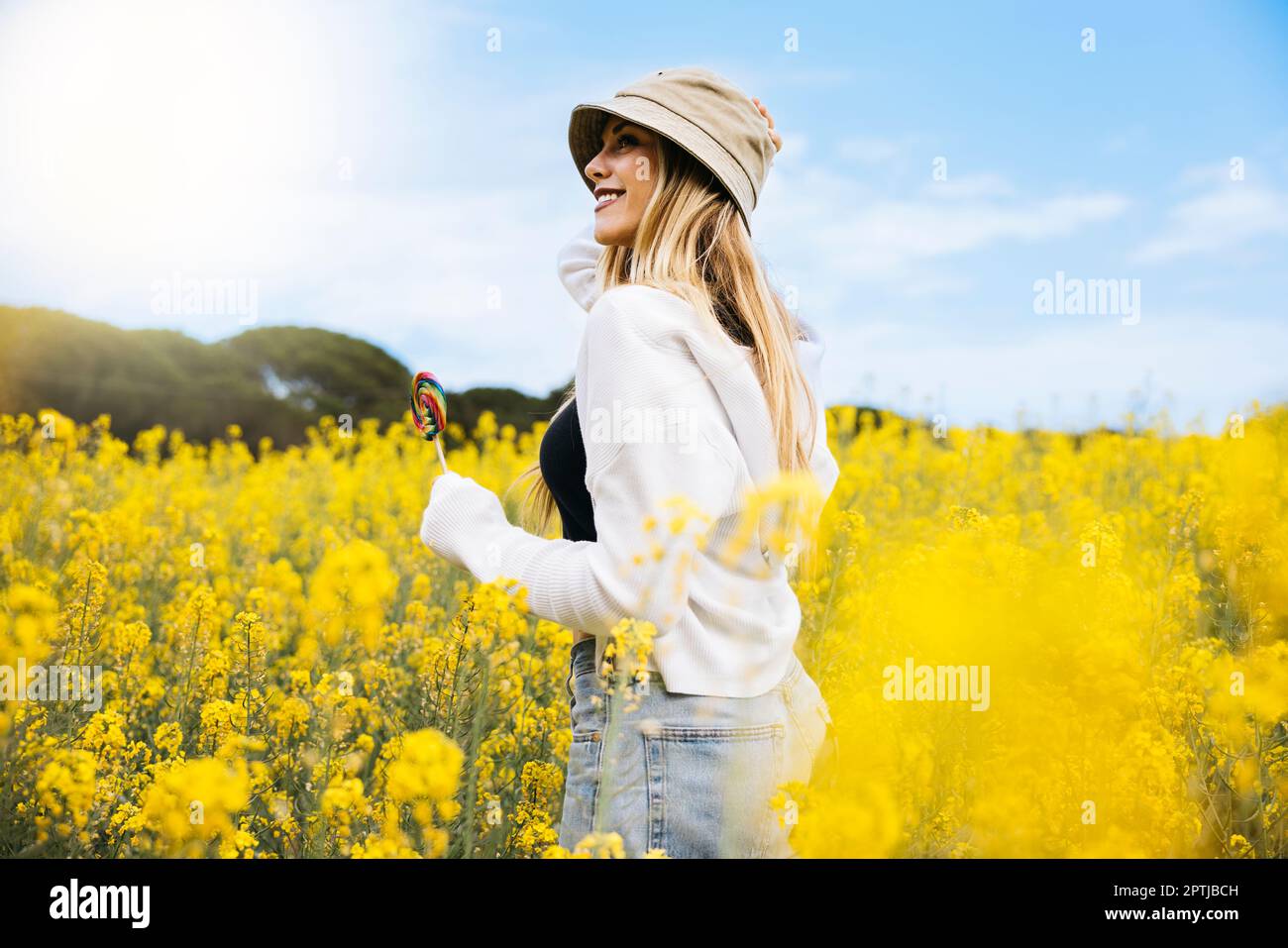 Bella ragazza dai capelli biondi posa in mezzo a un campo di fiori di colza gialli fiorenti Foto Stock