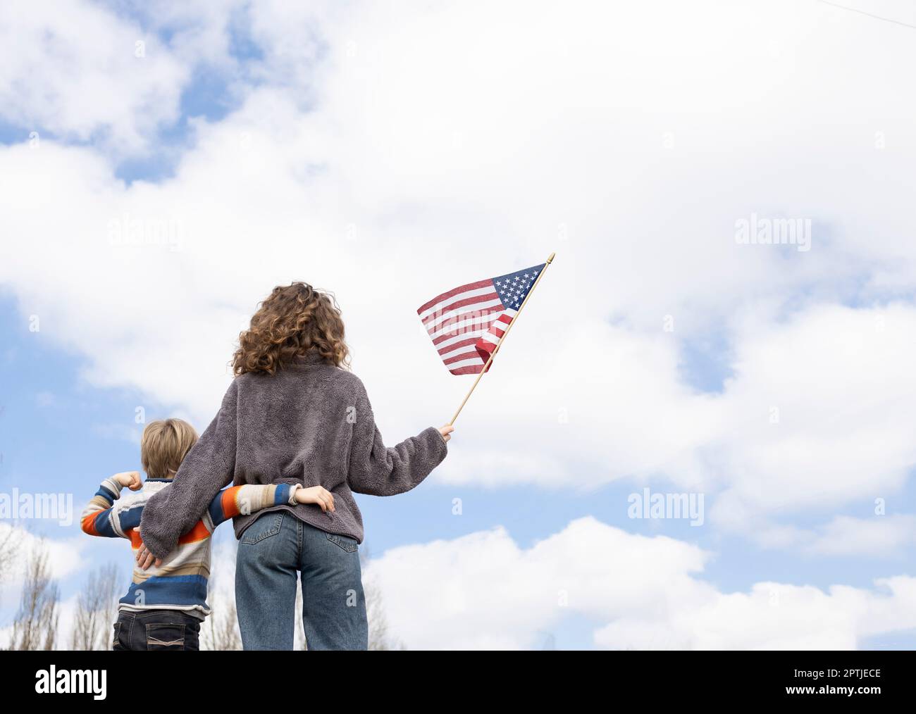 un ragazzo e una giovane donna irriconoscibili si alzano con le spalle tenendo la bandiera americana contro il cielo Foto Stock
