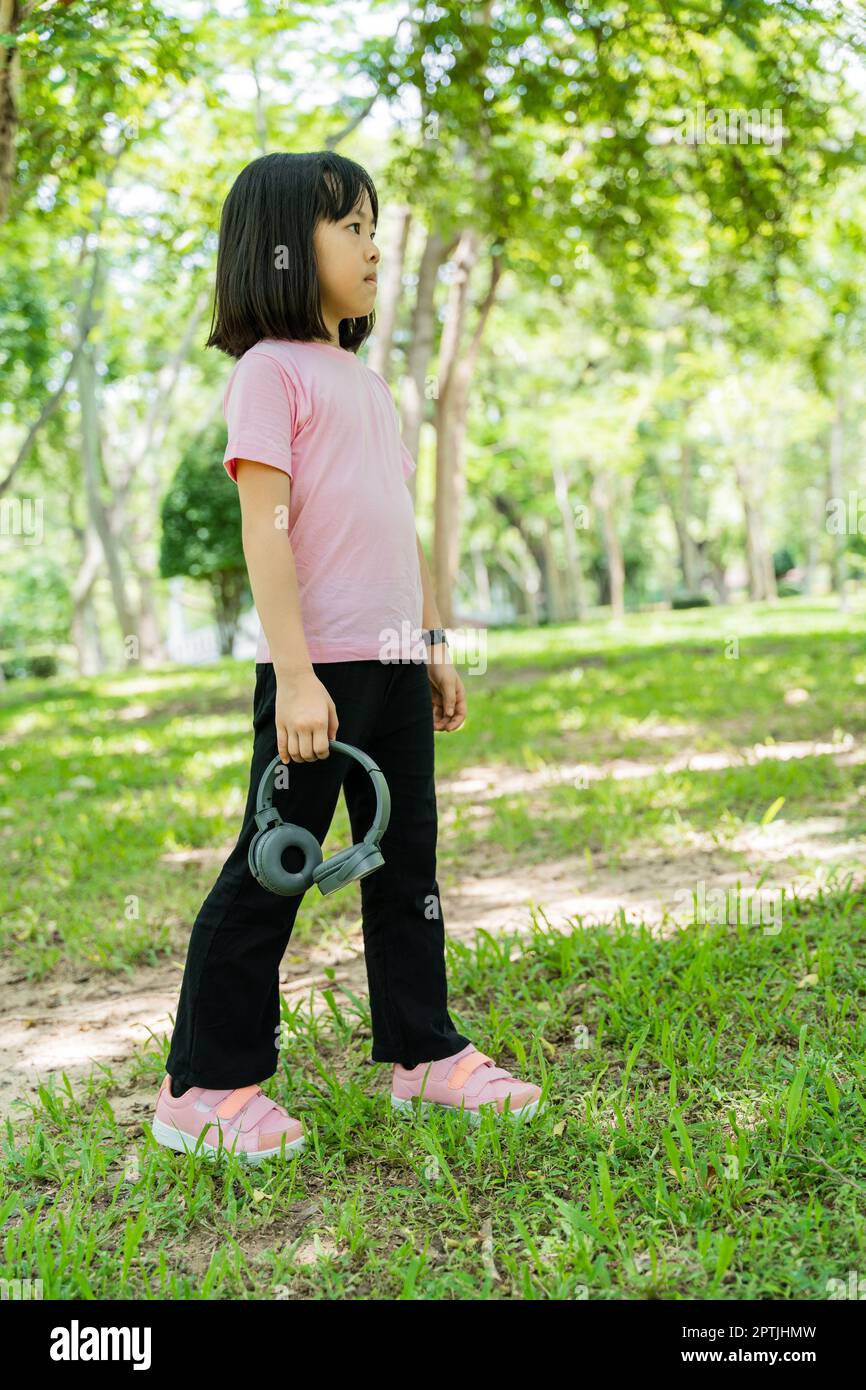 Ritratto di bambina ascolta la musica con le cuffie moderne senza fili nel verde parco all'aperto. Foto Stock