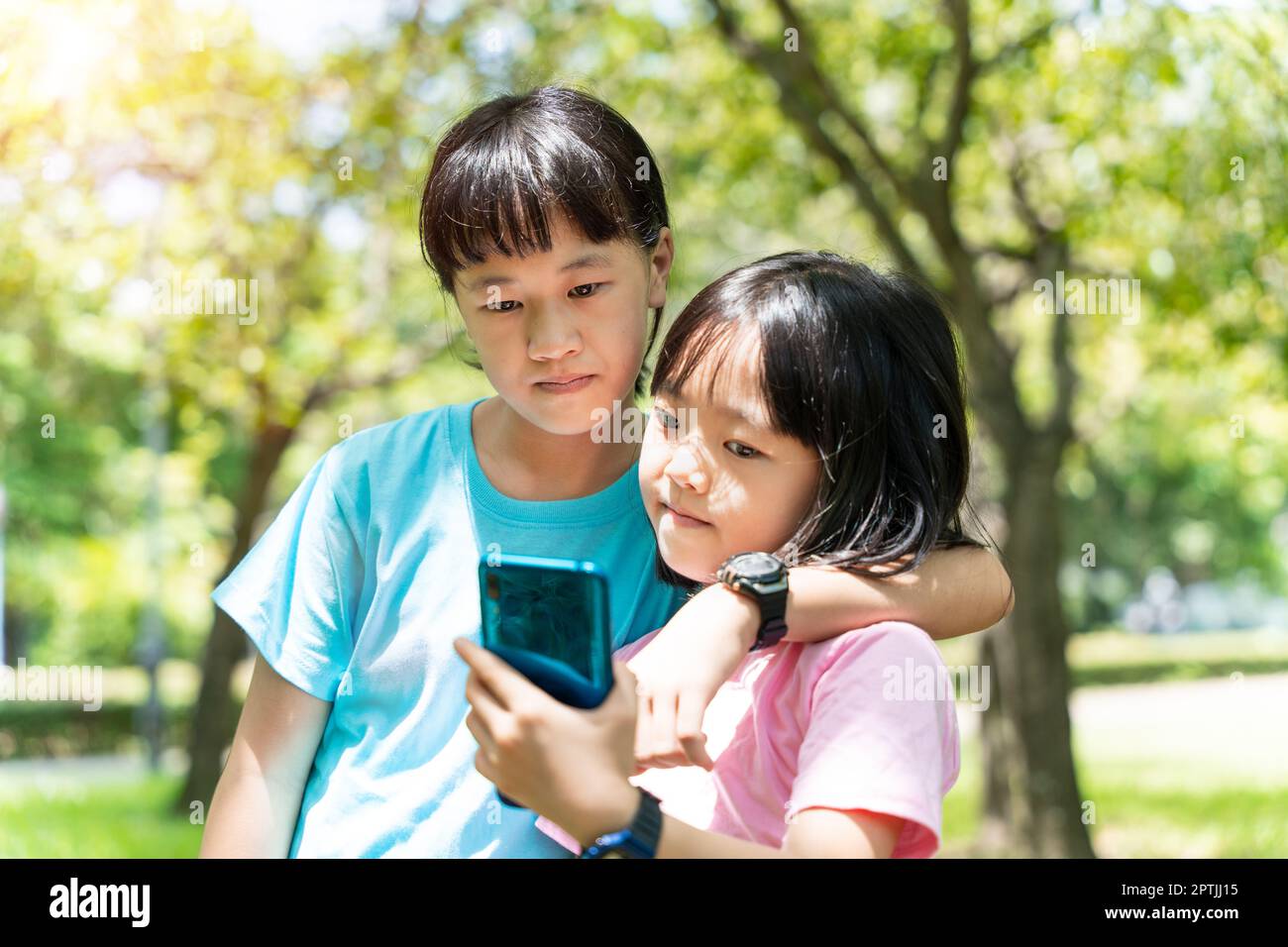 Due sorelle che abbraccia mentre usano il telefono cellulare nel parco. Felice concetto di famiglia. Foto Stock