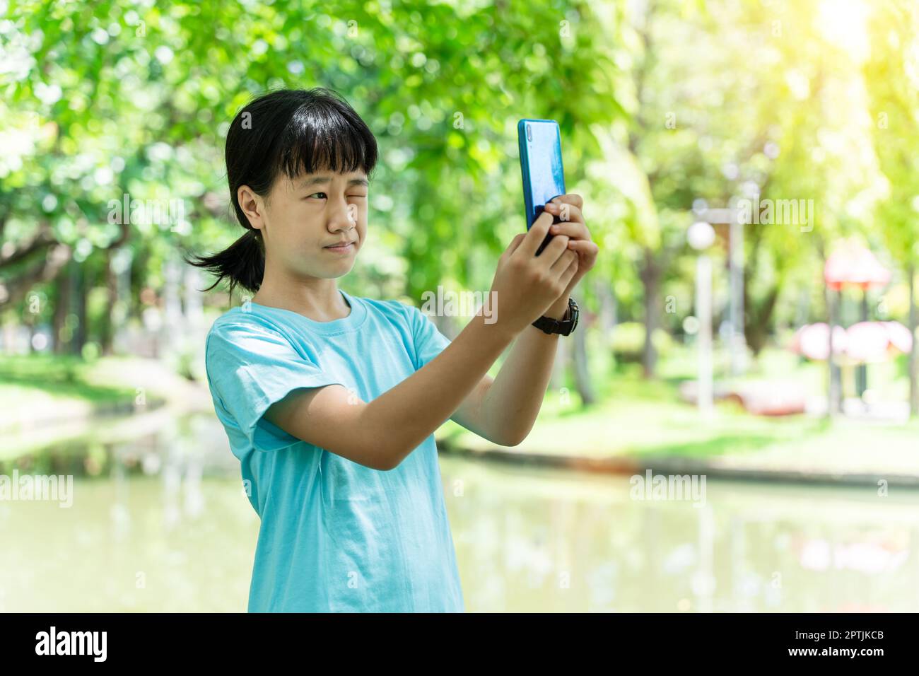 ritratto di una giovane bambina asiatica che utilizza smartphone mobile mentre si trova nel parco in una calda giornata primaverile. Foto Stock