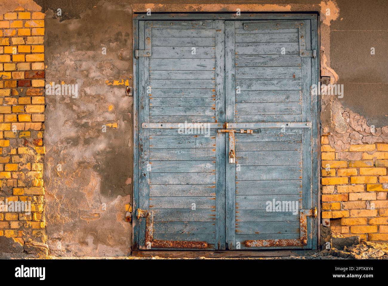 Vecchia porta chiusa con un lucchetto, sullo sfondo di un vecchio muro di pelatura. Mattoni e crepe sul muro. Vista frontale. Foto Stock