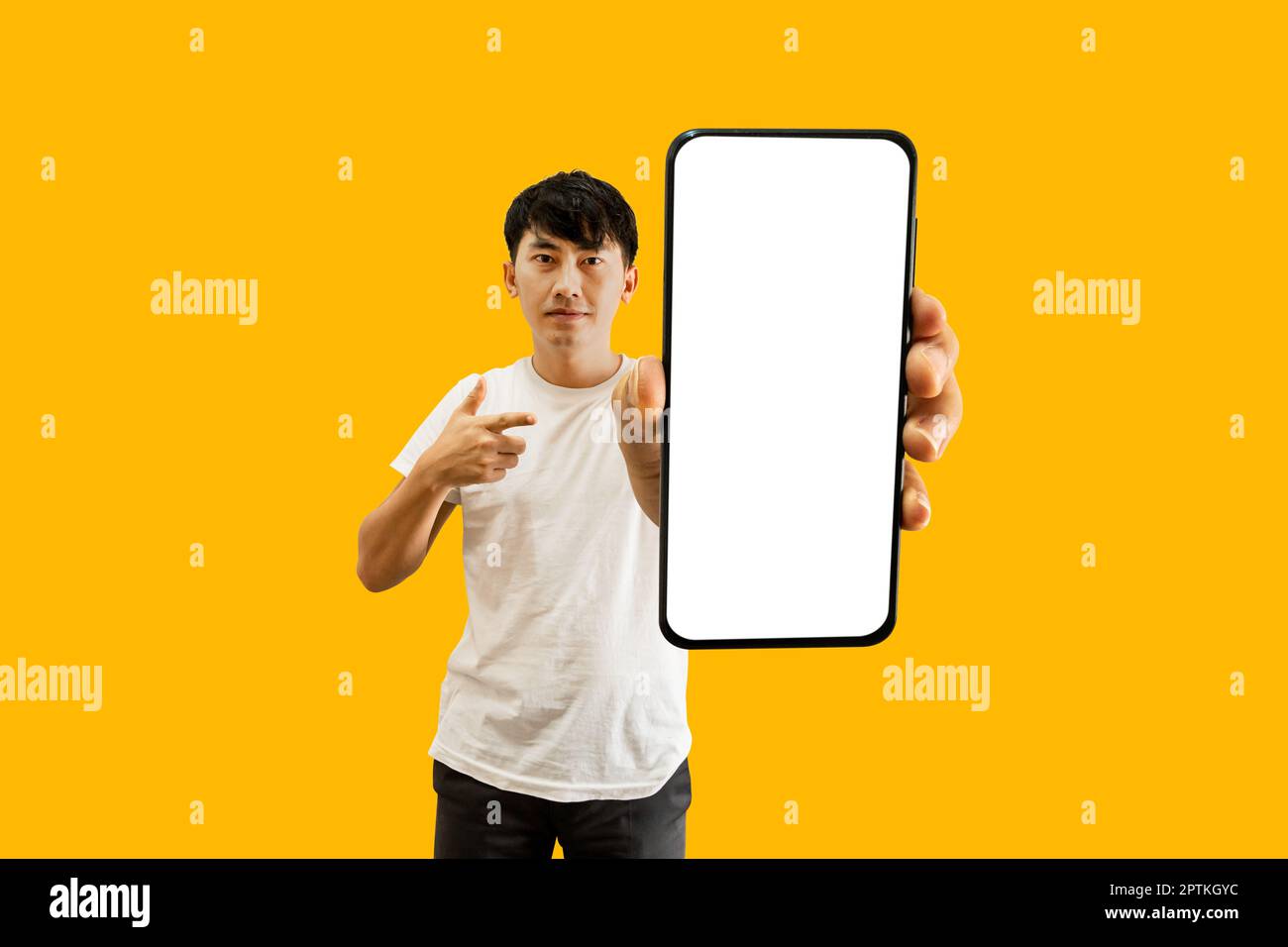 Mano dell'uomo asiatico che indica lo schermo bianco vuoto dello smartphone su sfondo giallo. Cellulare Display Mock Up per la pubblicità app mobile. Foto Stock