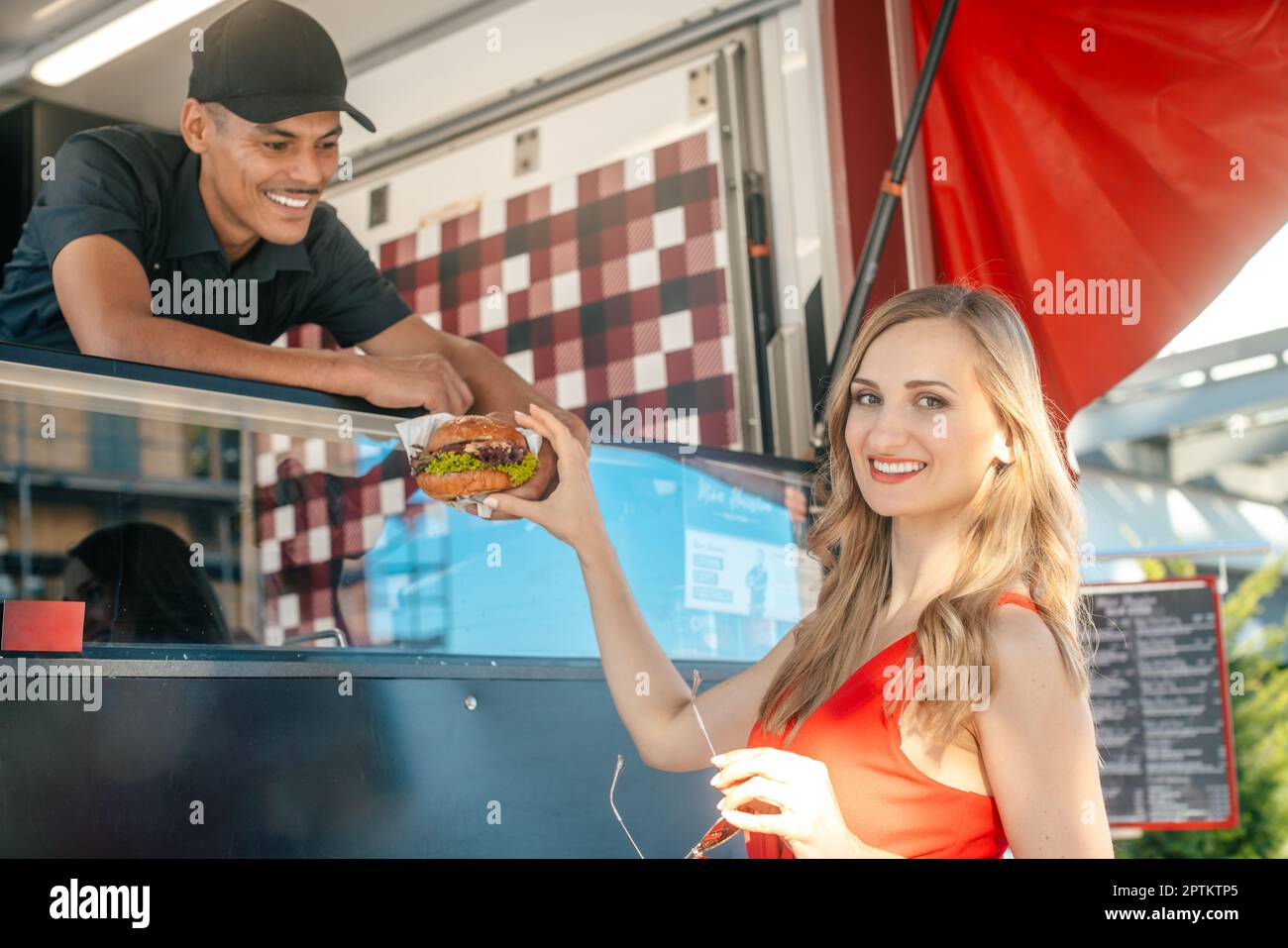 Friendly Cook in un camion alimentare che consegna hamburger gustosi sopra alla donna cliente Foto Stock