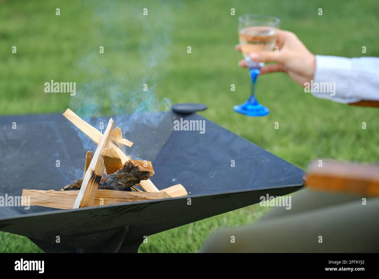 Legna da ardere alla griglia all'aperto e mano sfocata con un bicchiere di limonata sullo sfondo Foto Stock