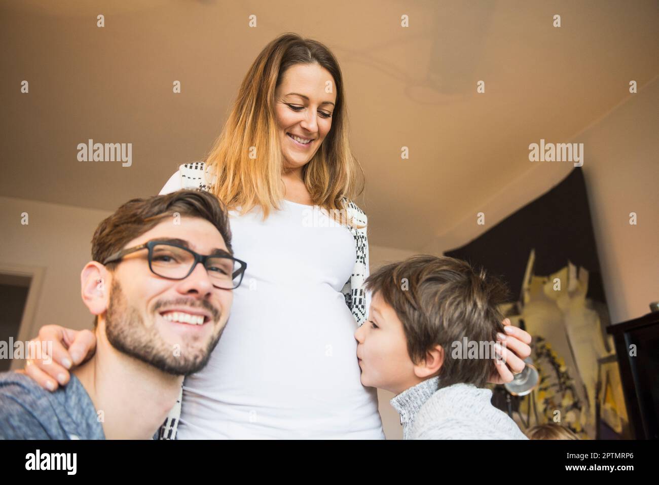 Ragazzo baciando il ventre di madre incinta mentre il padre guarda la macchina fotografica, Monaco, Germania Foto Stock