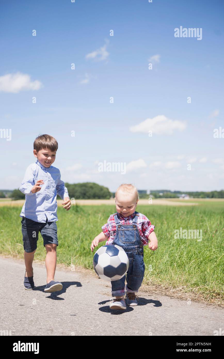 Bambino che gioca a calcio con il fratello su un prato in campagna, Baviera, Germania Foto Stock